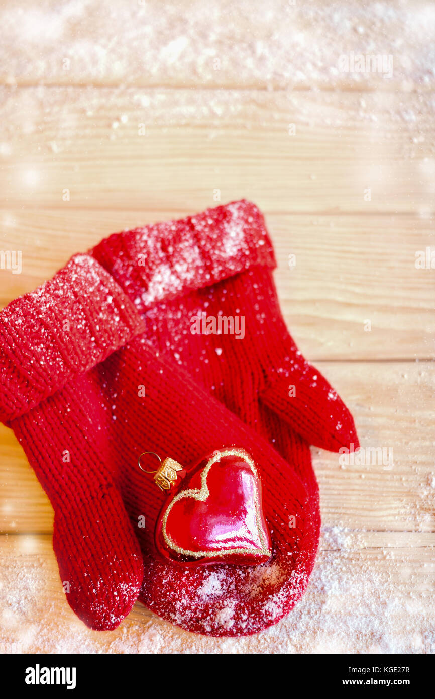 Weihnachten Spielzeug Herz auf Rot gestrickte Handschuhe auf Holztisch mit Schnee. Stockfoto