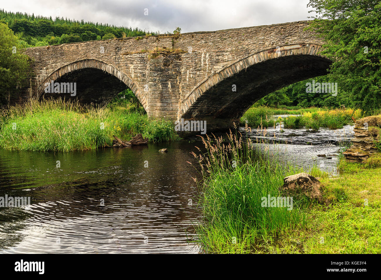 Alte Steinbrücke über den Fluss Dee in Wales, Vereinigtes Königreich. Typisch walisische Landschaft in trüben Sommertag. Ruhige romantische Atmosphäre. Stockfoto