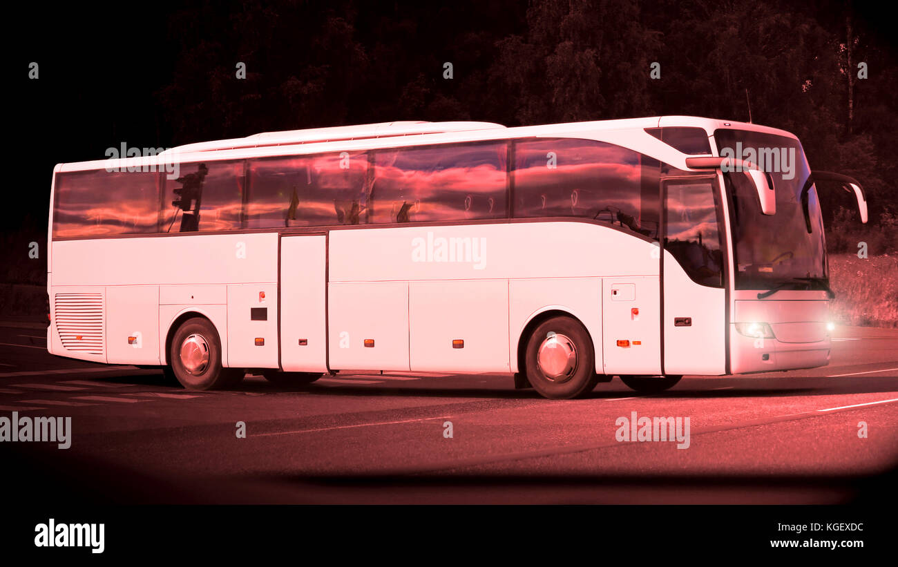 Weißer Bus fährt auf seiner Reise in den späten Abend bei Sonnenuntergang Reflexionen auf der Seite. Stockfoto