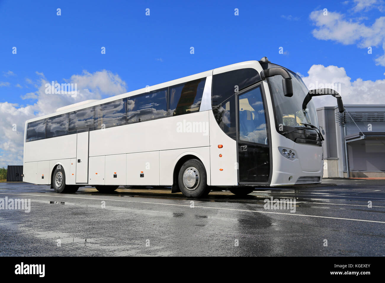 Weißer Bus wartet an einem Sommertag mit nassem reflektierendem Asphalt und blauem Himmel mit Wolken an der Bushaltestelle auf Passagiere. Stockfoto
