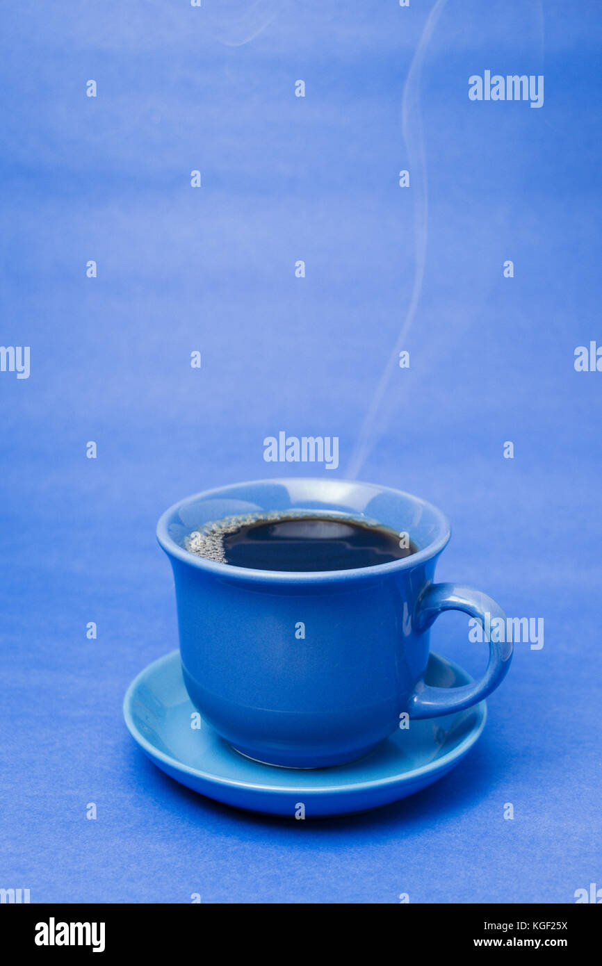 Blauer Becher mit dampfendem heißem Kaffee. Weicher Rauch. Blauer Hintergrund. Vertikales Foto Stockfoto