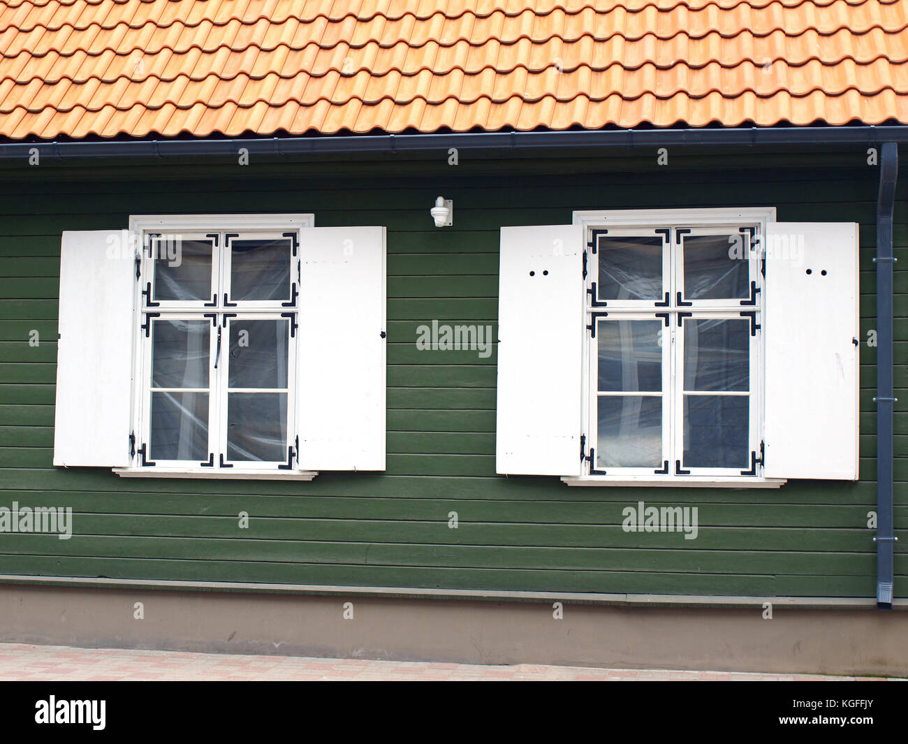 Zwei Retro Stil weiß Holzfenster mit Rollläden auf grünem Holz- Haus Wand- und roten Lehm Ziegeldach Stockfoto