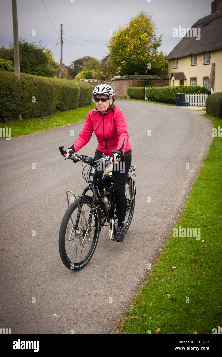 65 Jahre alte weibliche Radfahrer auf einer ländlichen Straße, in der Ortschaft Shapwick, Dorset. Stockfoto