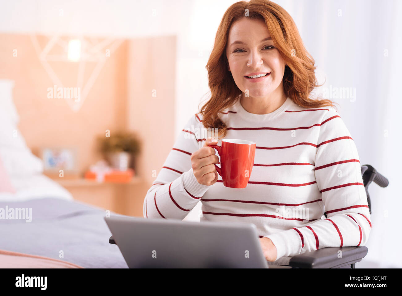 Freudige behinderte Frau mit Ihrem Laptop und einem Becher Stockfoto