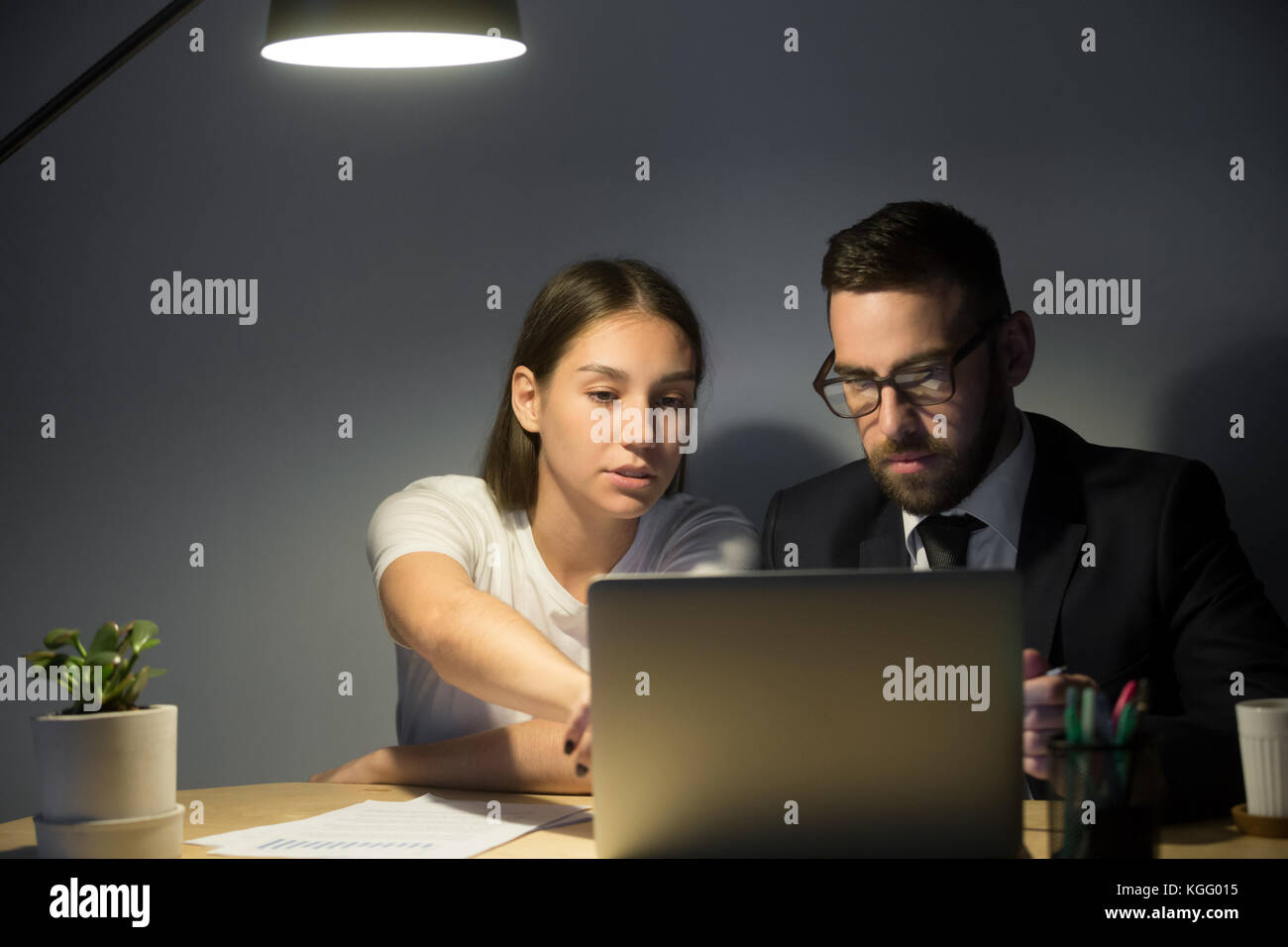 Zwei schwere Kollegen arbeiten auf ein Problem am späten Abend treffen. weiblichen Trainer zeigen männliche Mitarbeiter wichtige Projektdetails in Laptop s Stockfoto