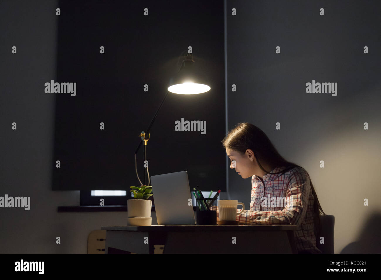 Lässige junge erwachsene Frau Studie online für Universität Projekt, Notizen zu machen. Prüfung Schüler Vorbereitung Test alleine im dunklen Zimmer mit Lampe Licht Stockfoto