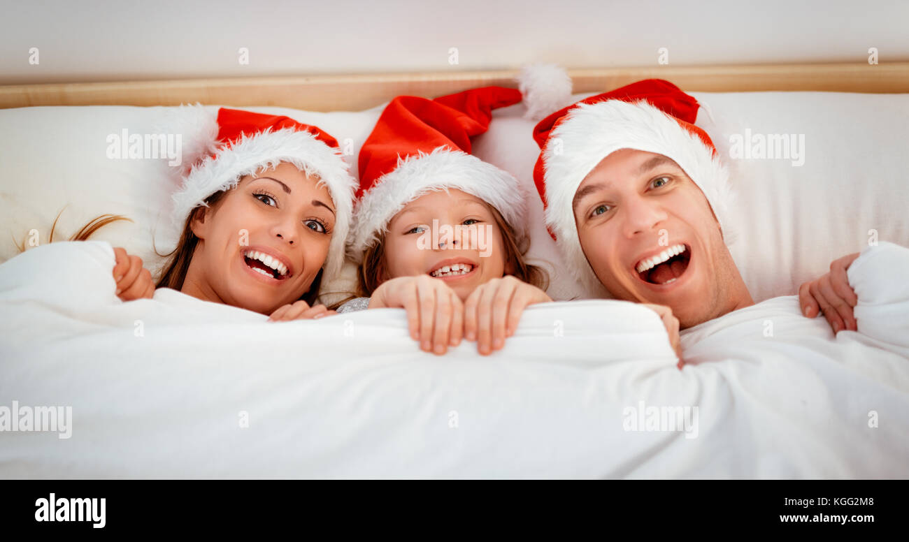 Schönen lächeln Familie mit Santa hat Spaß im Bett. Sie im Bett liegen an Kamera und peeking unter der Decke mit einem Lächeln. Stockfoto