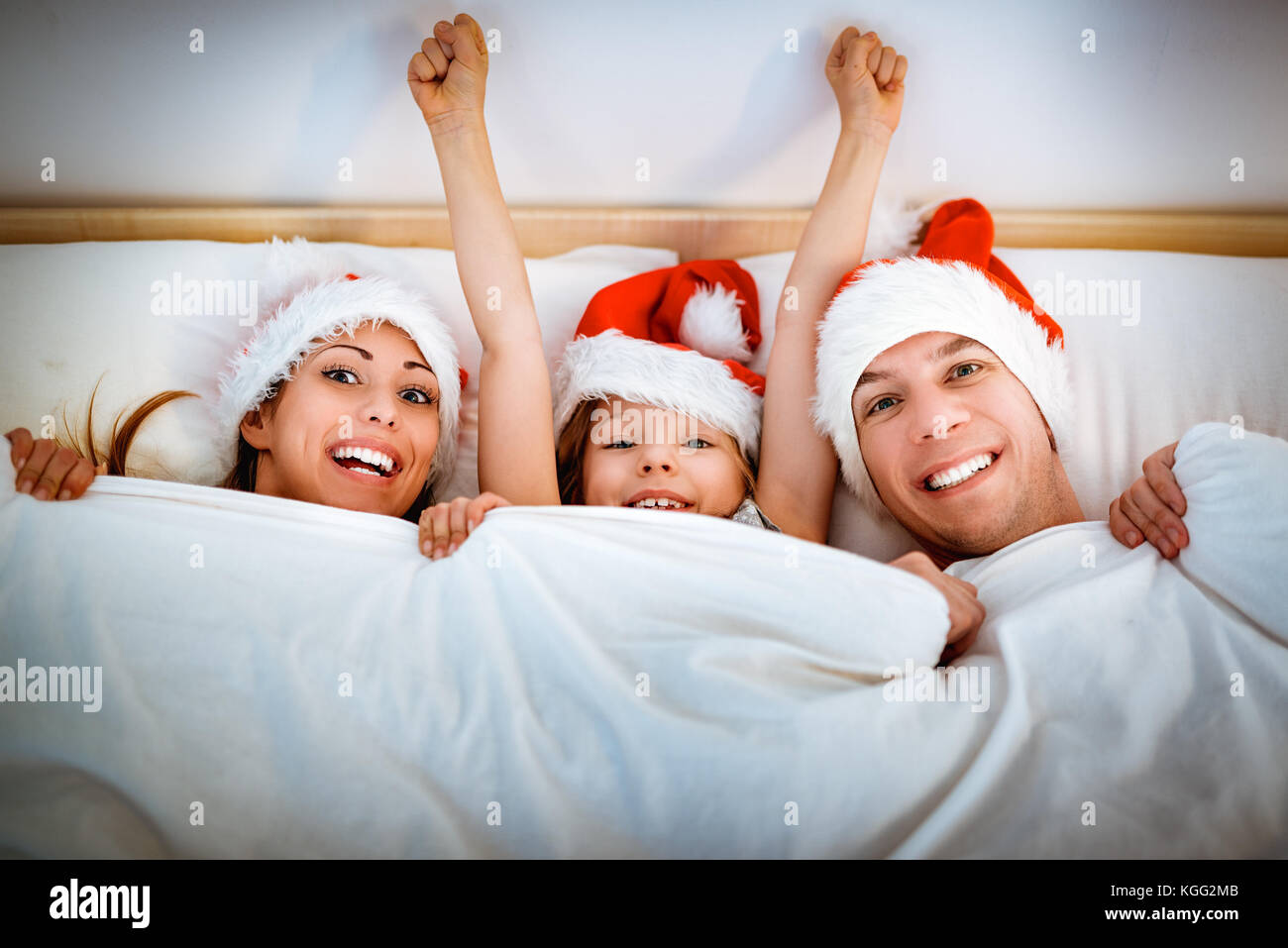 Lächelnd glücklich Mama, Papa und kleines Mädchen in roten Hüte in weißen Bett lag, durch die Decke abgedeckt und Spaß haben. Stockfoto