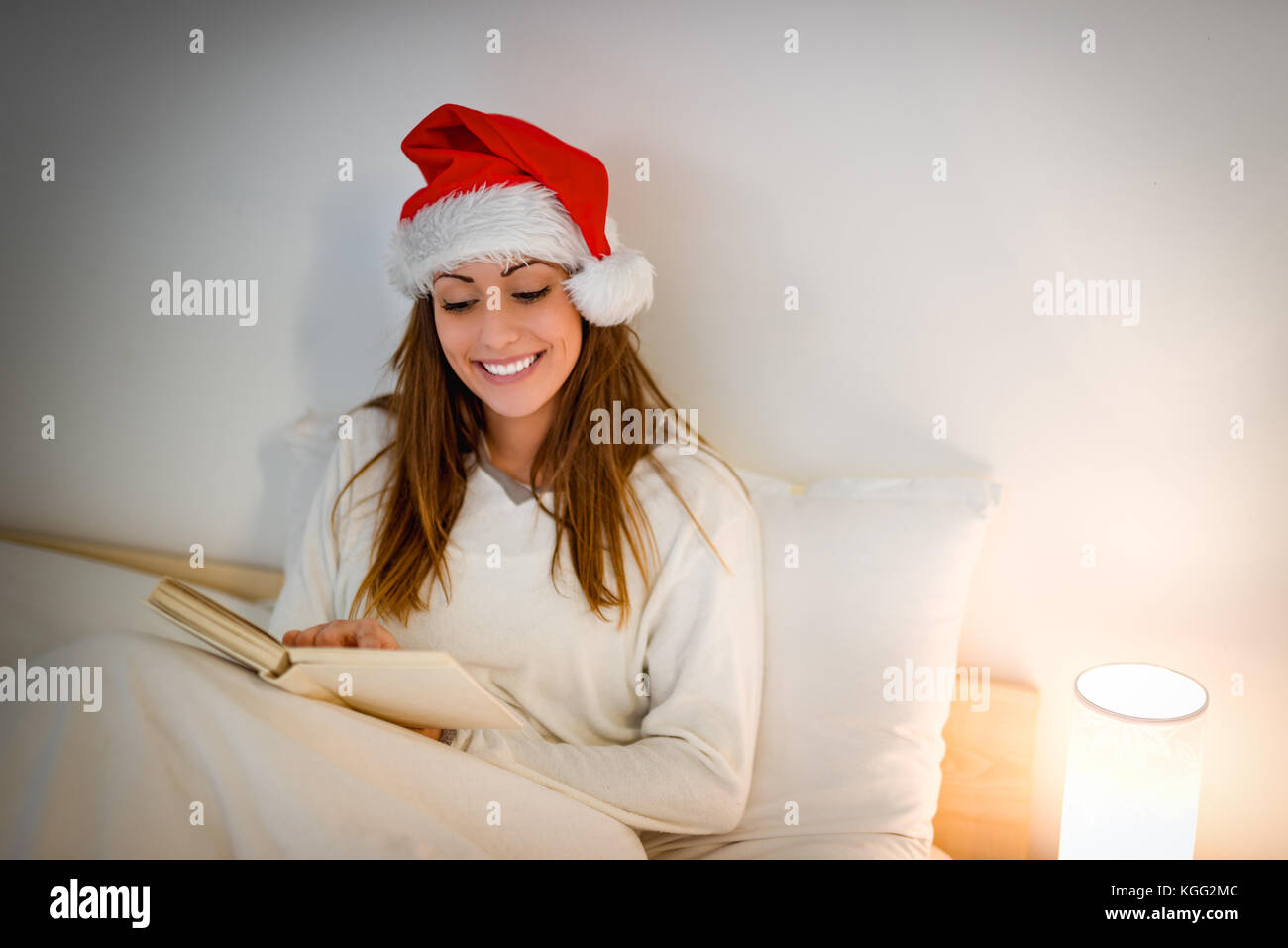 Schöne lächelnde Mädchen in weißen gemütlichen Bett und liest ein Buch warten auf Weihnachten. Stockfoto