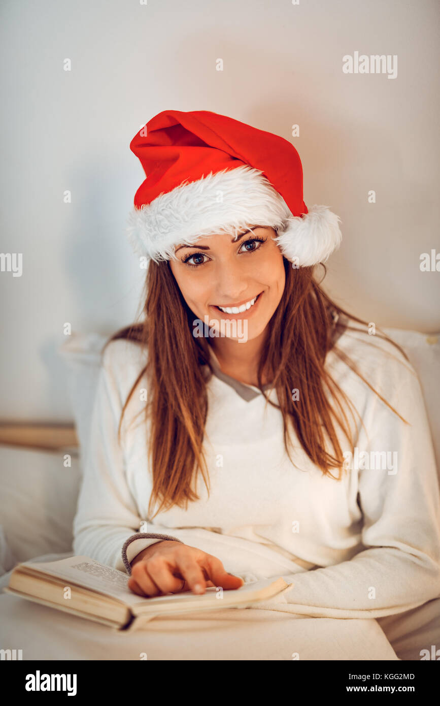 Schöne lächelnde Mädchen mit weihnachtsmütze Entspannen in gemütlichen Bett und Lesen Buch. Bei Kamera schaut. Stockfoto