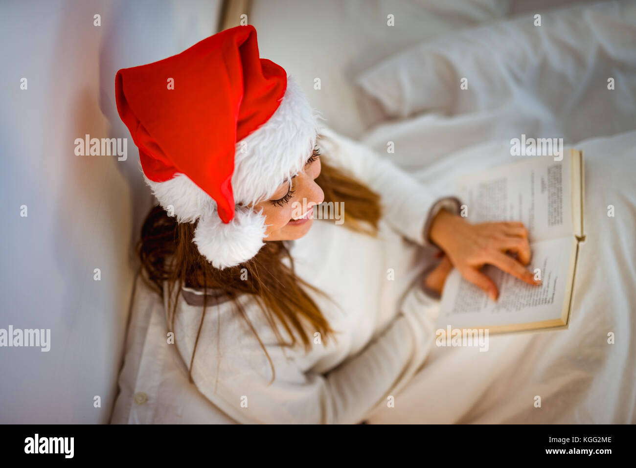 Ansicht von oben eine schöne lächelnde Mädchen mit weihnachtsmütze Entspannen in gemütlichen Bett und Lesen Buch. Stockfoto