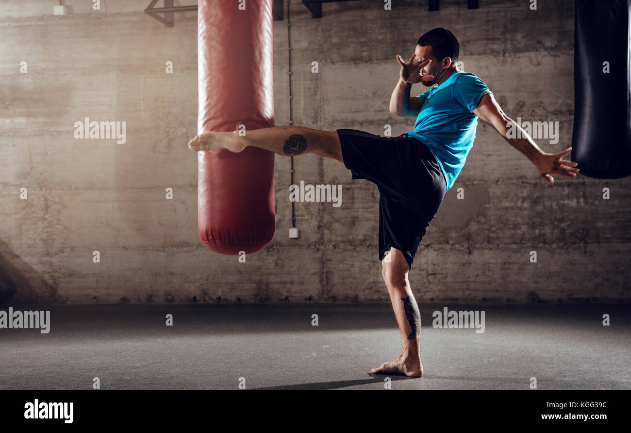 Muskulöse mann Stanzen mit Bein ein Boxsack auf Cross fit Training im Fitnessstudio. Stockfoto