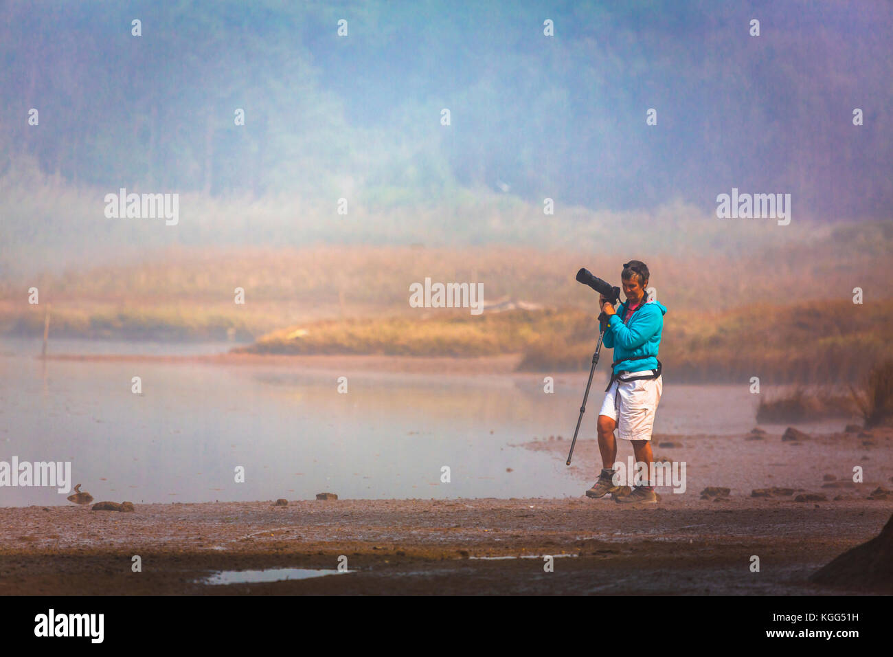 Fotografin mit Kamera und Monopod am Rande einer nebligen Lagune von Óbidos, Portugal Stockfoto