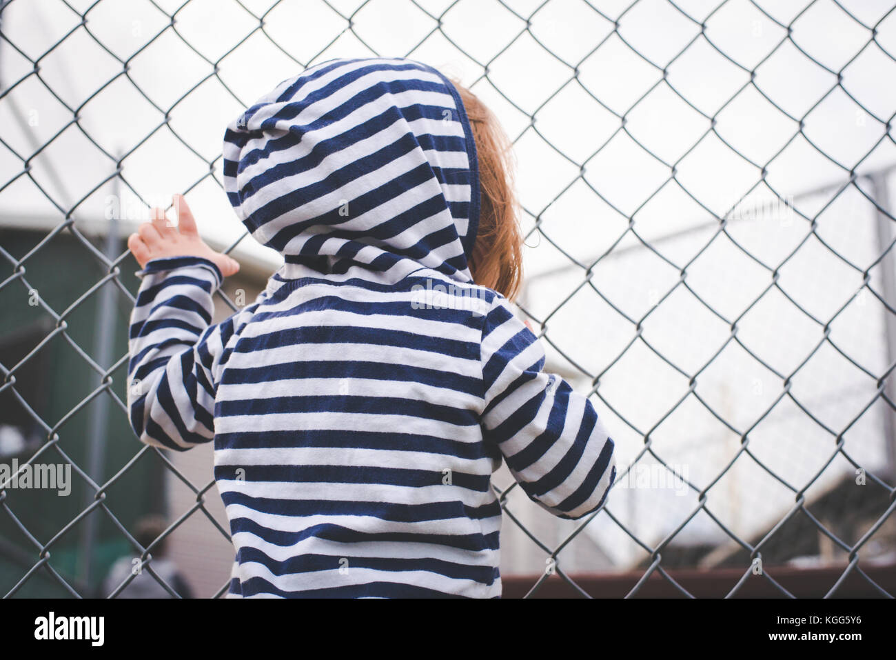 Das Kind hängt an einem Zaun und schaut durch ihn. Stockfoto