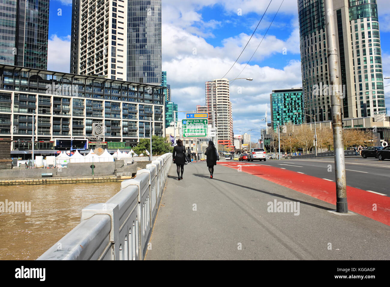 Zwei weibliche junge Erwachsene gehen auf eine Brücke über den Fluss Yarra in Melbourne, Australien, Ansicht auf einem Wolkenkratzer Stockfoto