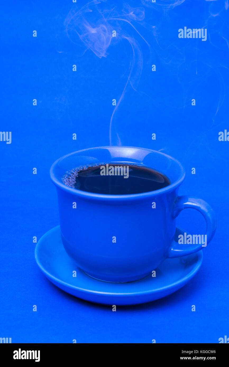 Blauer Becher mit dampfendem heißem Kaffee. Weicher Rauch. Blauer Hintergrund. Vertikales Foto Stockfoto
