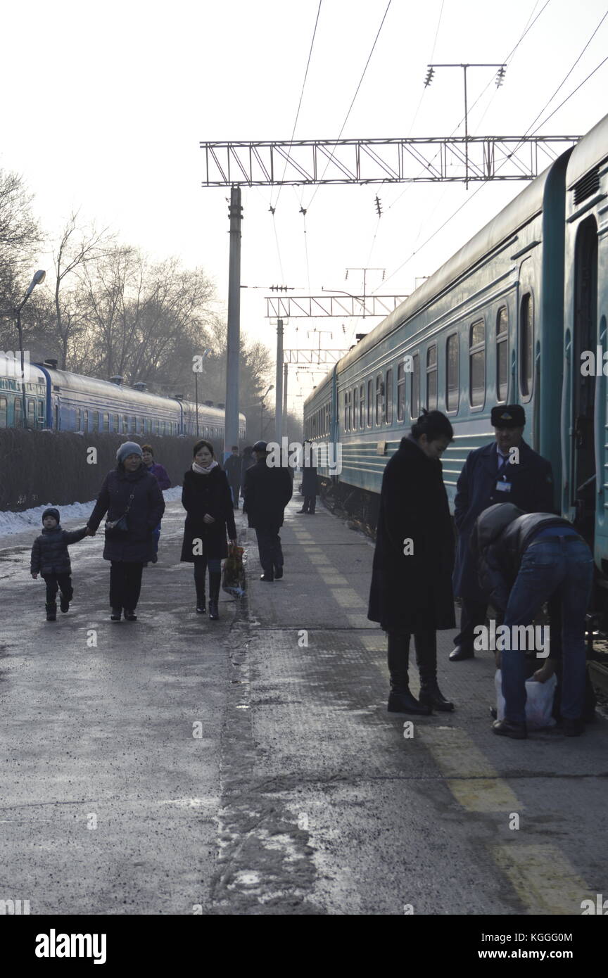 Russischer Zug in Kasachstan im Winter, Menschen, die auf dem Bahnsteig gehen und aus dem Zug aussteigen. Zug Dirigent, prowodnik, mit uschanka, Pelzhut. Stockfoto