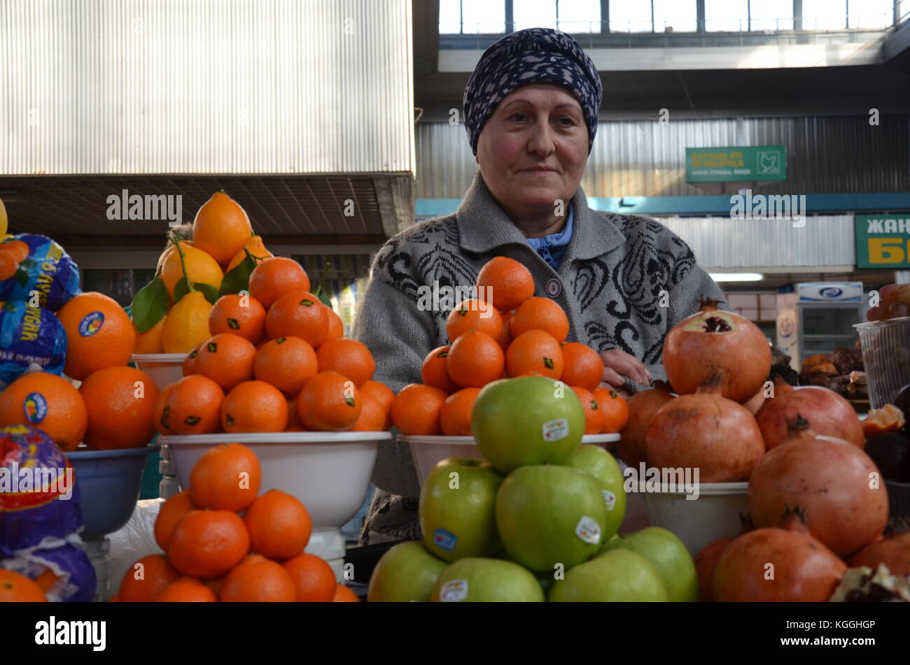 Hallenmarkt / Basar in almaty, kasachstan. Eine kasachische Frau und ein Mann verkaufen Lebensmittel auf dem Basar. Mandarinen, Nüsse, Trockenfrüchte, Äpfel Stockfoto
