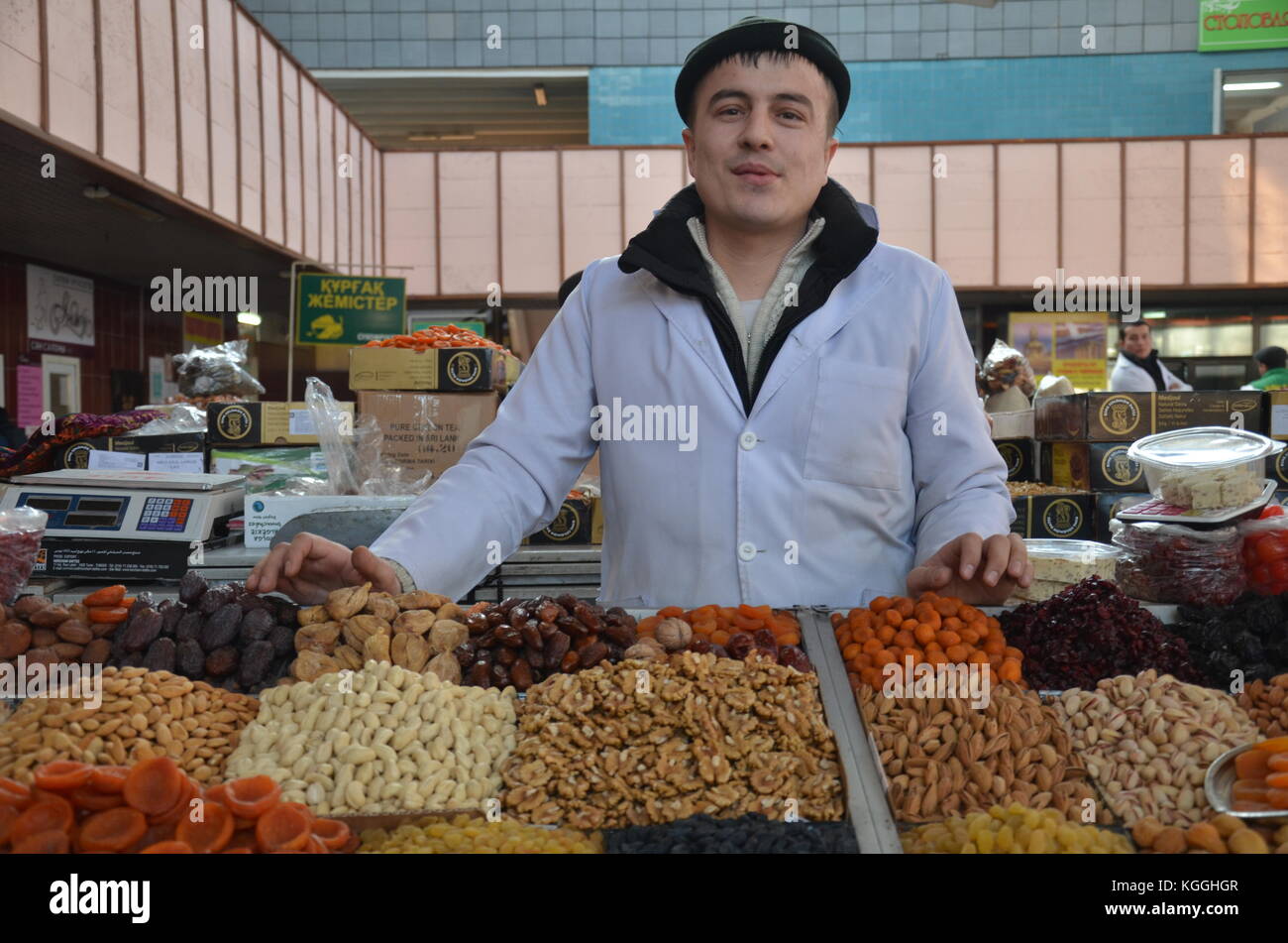 Hallenmarkt / Basar in almaty, kasachstan. Eine kasachische Frau und ein Mann verkaufen Lebensmittel auf dem Basar. Mandarinen, Nüsse, Trockenfrüchte, Äpfel Stockfoto