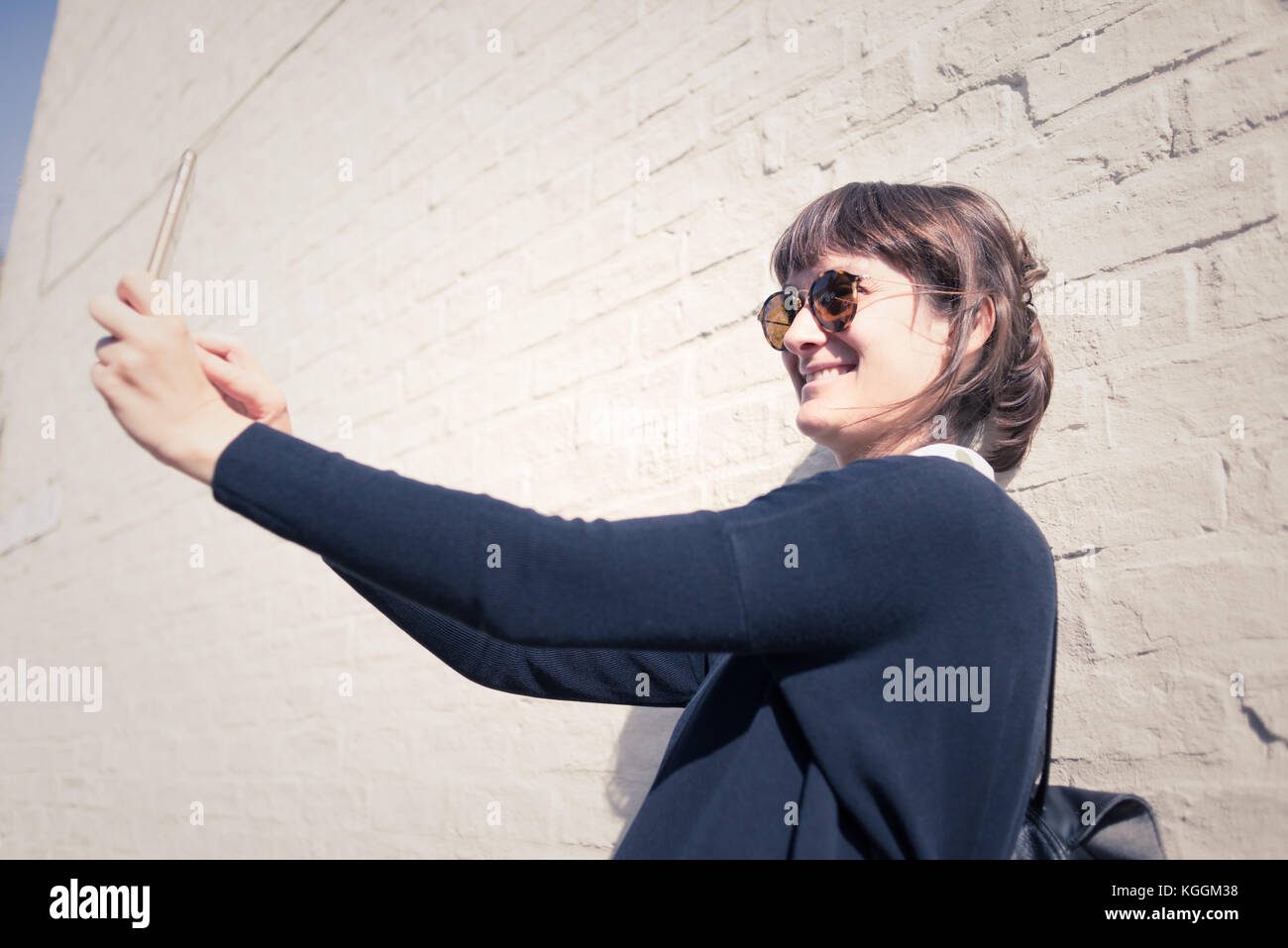 Junge Frau mit Sonnenbrille lächelnd und selfie vor eine weiße Wand als Hintergrund. Vintage Effekt Stockfoto