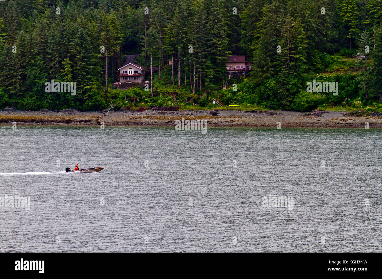 Ein kleines Boot Geschwindigkeiten hinter einer Gruppe von Häusern am Ufer in der Nähe von Juneau, Alaska. Stockfoto
