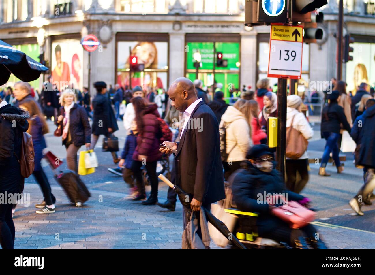 Mann, der das Handy überprüft, während Weihnachtseinkäufer ihn unbemerkt vorbeifahren, Oxford Circus, London, Großbritannien, 2017 Stockfoto
