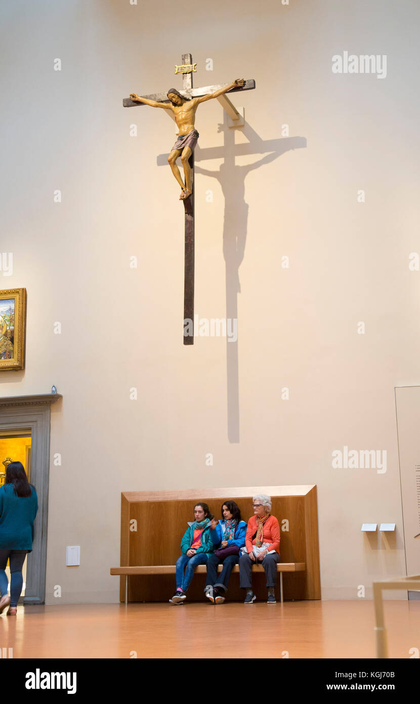 Drei Touristen aller Altersstufen auf einer Bank, auf das Innere des Museums unter einem Kruzifix Stockfoto