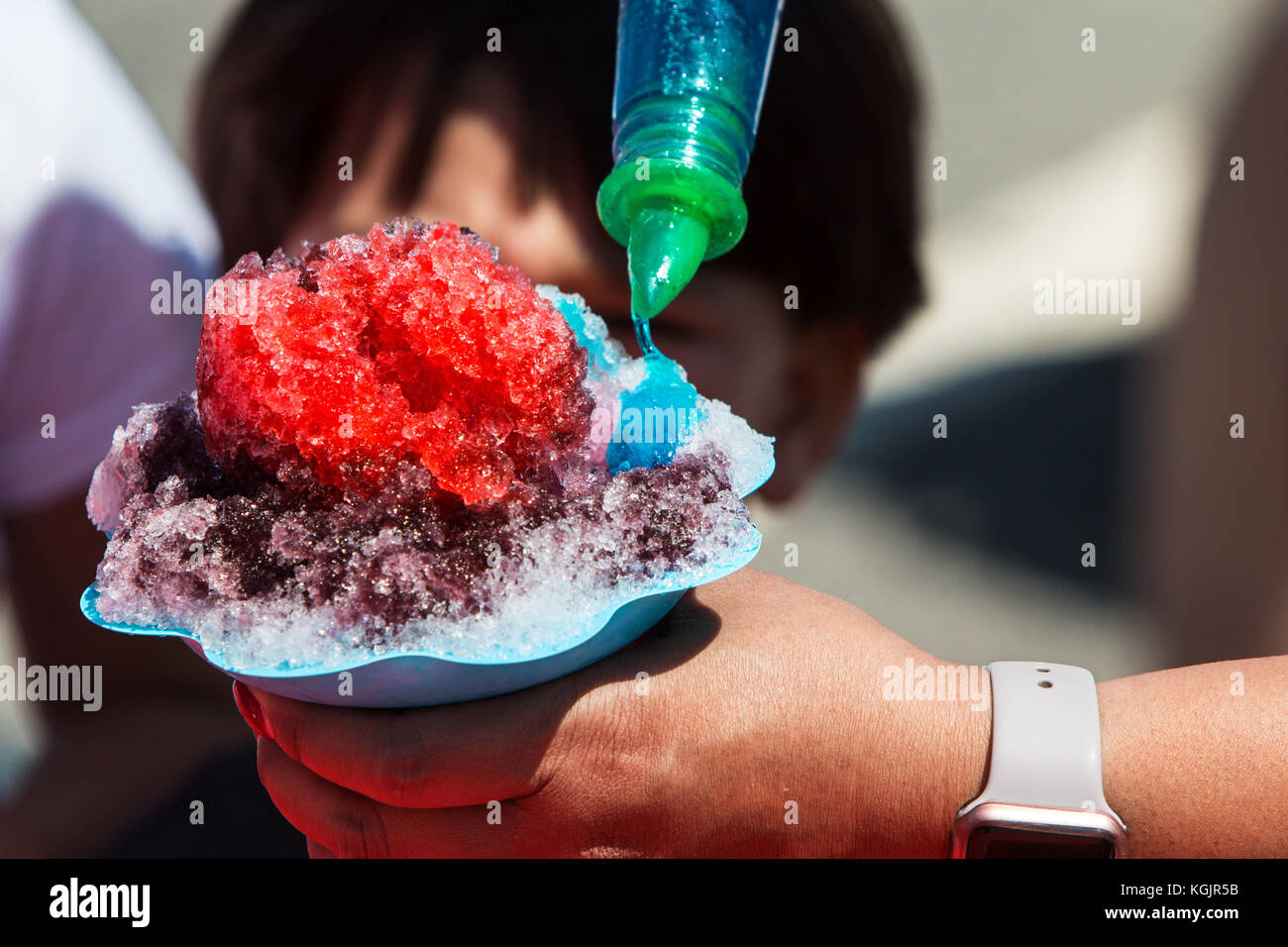 Nahaufnahme der Frau hand Schnee Kegel, wie sie Blue Sirup auf den crushed Eis gießt. Stockfoto