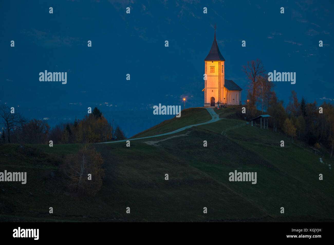 Jamnik, Slowenien - Blaue Stunde in Jamnik mit beleuchteter St. Primoz-Kirche. Julian Alpen im Hintergrund Stockfoto