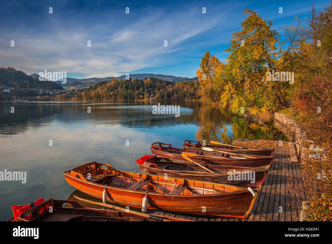 Bled, Slowenien - Traditionelle slowenische Boote am Bleder See mit bunten Herbstbäumen und blauem Himmel bei Sonnenuntergang Stockfoto