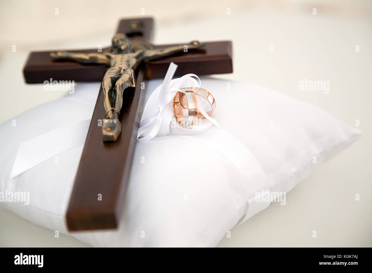 Hochzeit Ringe und kleine Holz- christliche Kreuz mit Christus auf weißen dekorative Kissen gelegt.jpg Stockfoto