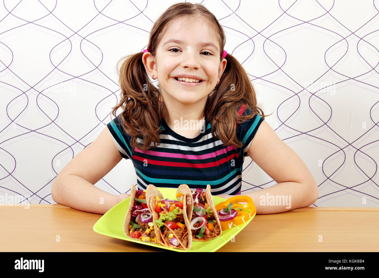 Glückliche kleine Mädchen mit Tacos auf Platte Stockfoto