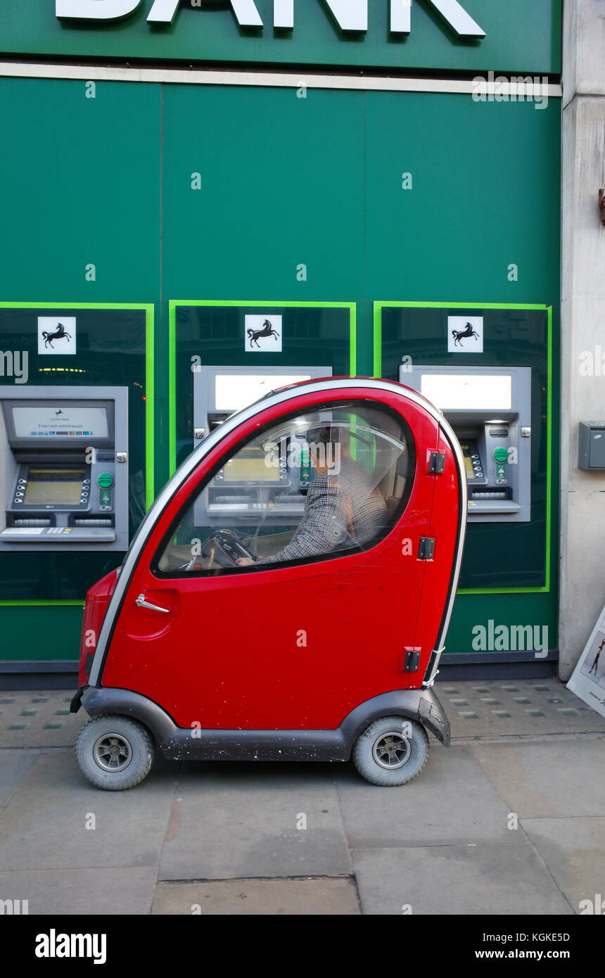 Mann in Rot Shoprider Mobilität scooter mit Geldautomaten Geldautomaten außerhalb Lloyds Bank in London, England Stockfoto