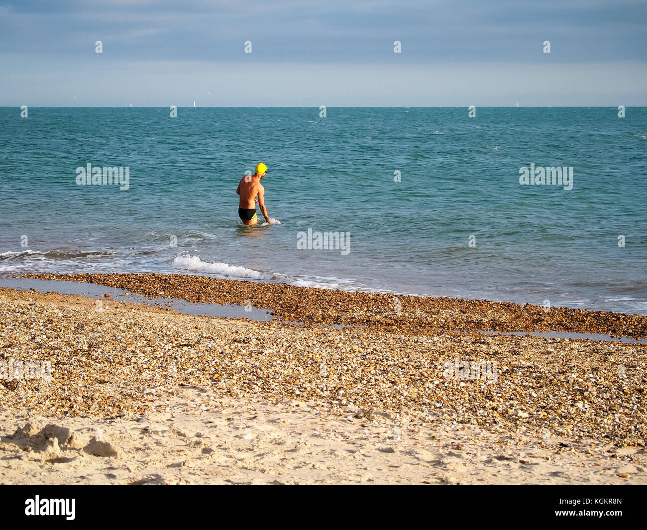 Ein Mann mit Badehose und Schwimmen hat watet in den Solent in einem autmn Tag Stockfoto
