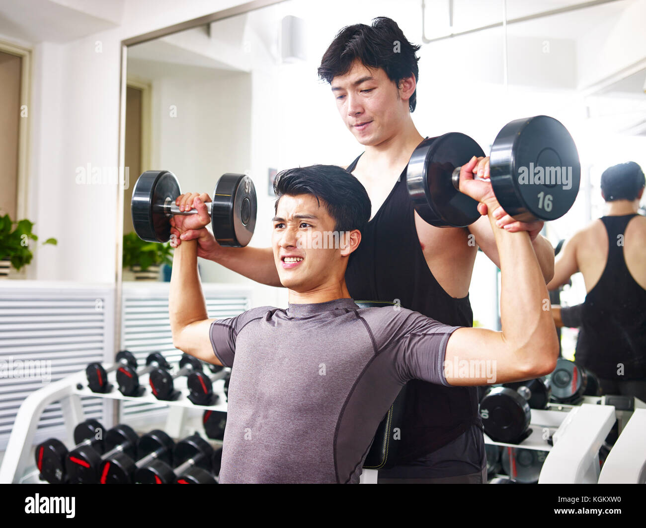 Asiatische junger erwachsener Mann durch Trainer trainiert, während Sie im Fitnessraum mit Hanteln. Stockfoto