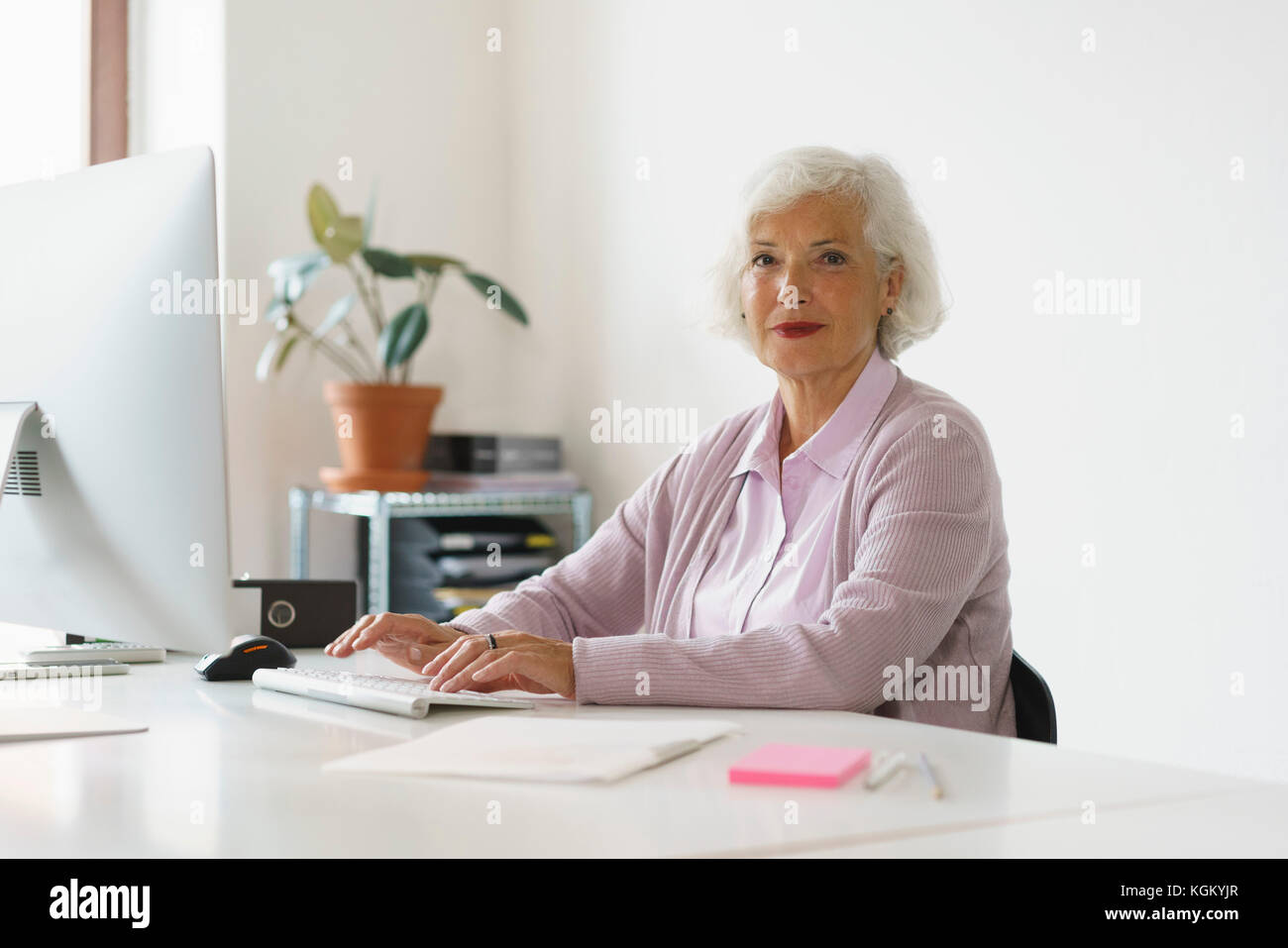 Porträt der lächelnde Frau mit Computer, während gegen die Wand im Büro zu sitzen Stockfoto