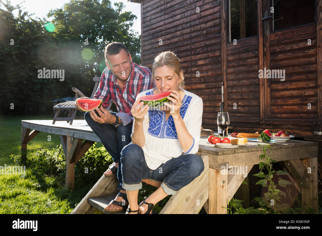 Gerne reifes Paar genießen Wassermelone Scheibe während der Sitzung außerhalb Bauernhaus an einem sonnigen Tag Stockfoto