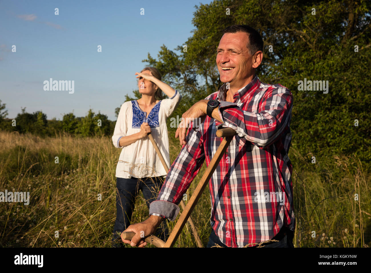 Lächelnd reifes Paar mit Ausrüstung stehen auf der Farm an einem sonnigen Tag Stockfoto