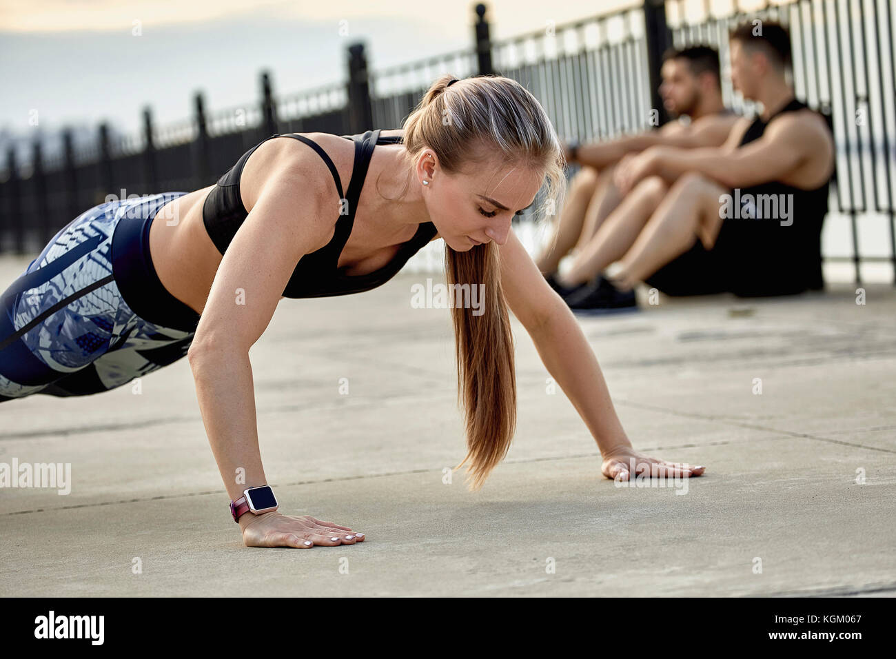 Junge weibliche Athleten üben Push-ups gegen männliche Freunde sitzen auf Fußweg Stockfoto