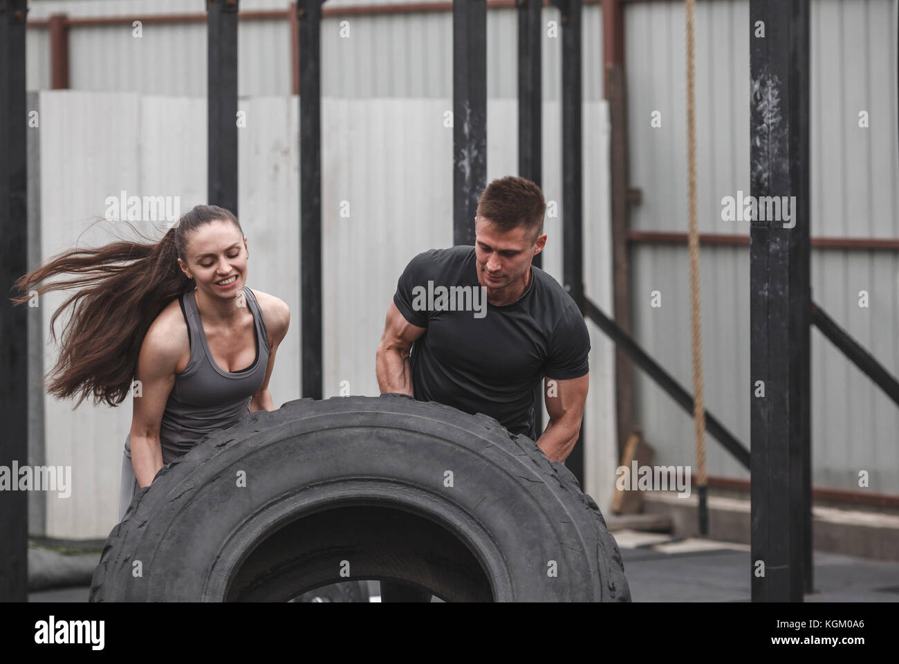 Männliche Kursleiter Unterstützung von weiblichen Athleten in Flipping Reifen im Fitnessstudio Stockfoto