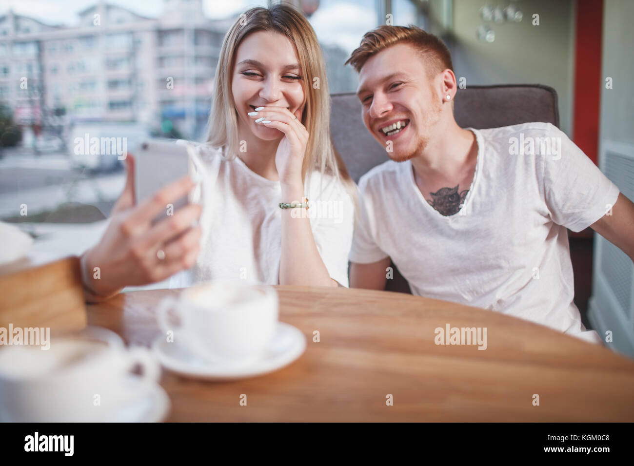 Glückliches junges Paar auf der Suche nach Handy während im Restaurant sitzen Stockfoto