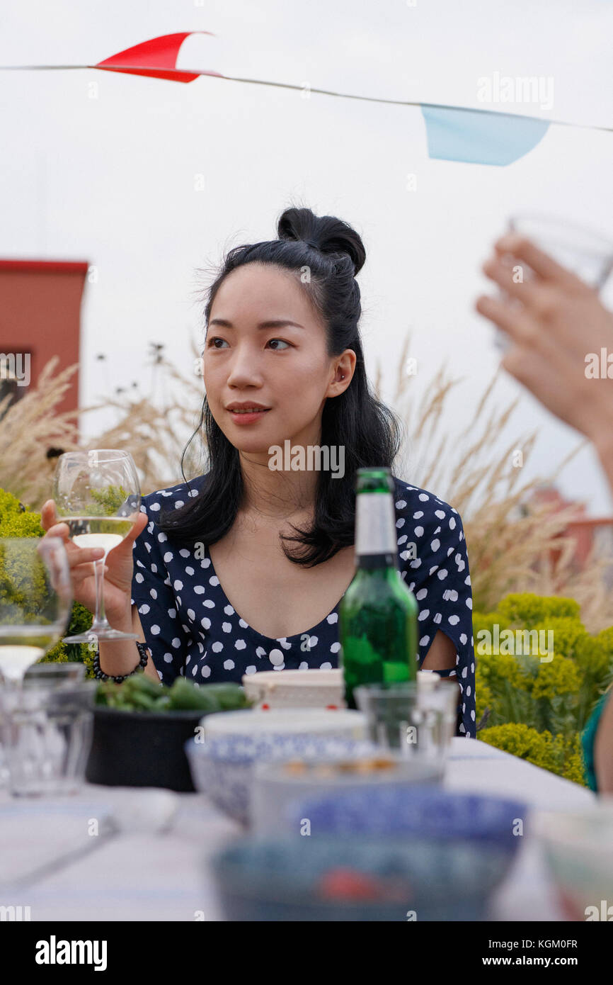 Nachdenkliche junge Frau mit Weinglas bei Tisch im Freien während der Partei sitzen Stockfoto