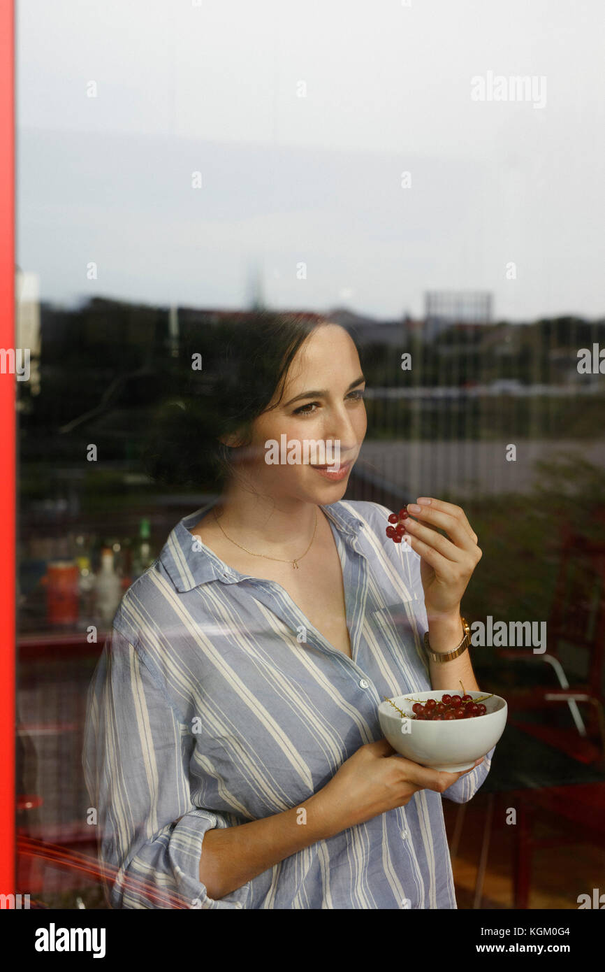 Nachdenkliche junge Frau essen Rote Johannisbeeren, während durch das Fenster suchen Stockfoto