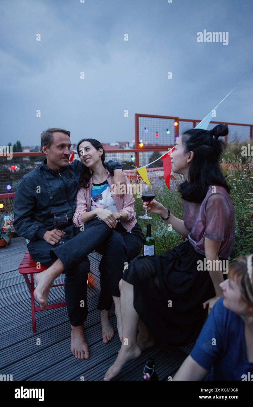 Glückliches Paar sprechen beim Sitzen mit Freunden auf der Terrasse in der Dämmerung Stockfoto