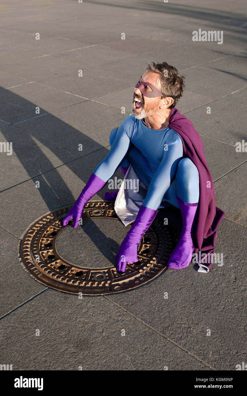 Hohe Betrachtungswinkel von Superhelden schreien beim Öffnen der kanaldeckel Deckel auf Wanderweg in Stadt Stockfoto