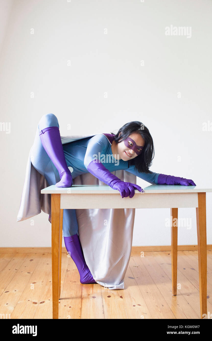 Junge weibliche Superheld Klettern am Tisch gegen weiße Wand Stockfoto