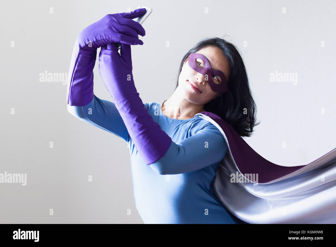 Junge Frau gekleidet als Superheld unter selfie vor weißem Hintergrund Stockfoto