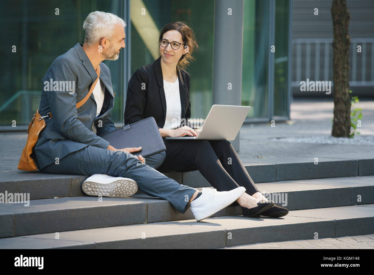 Unternehmen Mitarbeiter mit Laptop diskutieren beim Sitzen auf Schritte in der Stadt Stockfoto