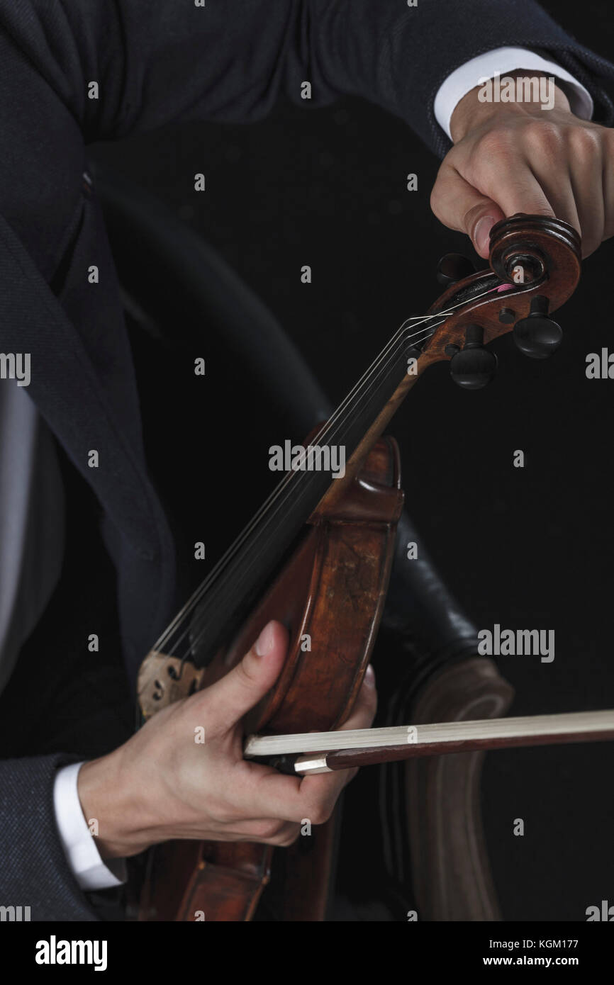 Zugeschnittenes Bild von geiger tuning Violine sitzend auf Stuhl Stockfoto