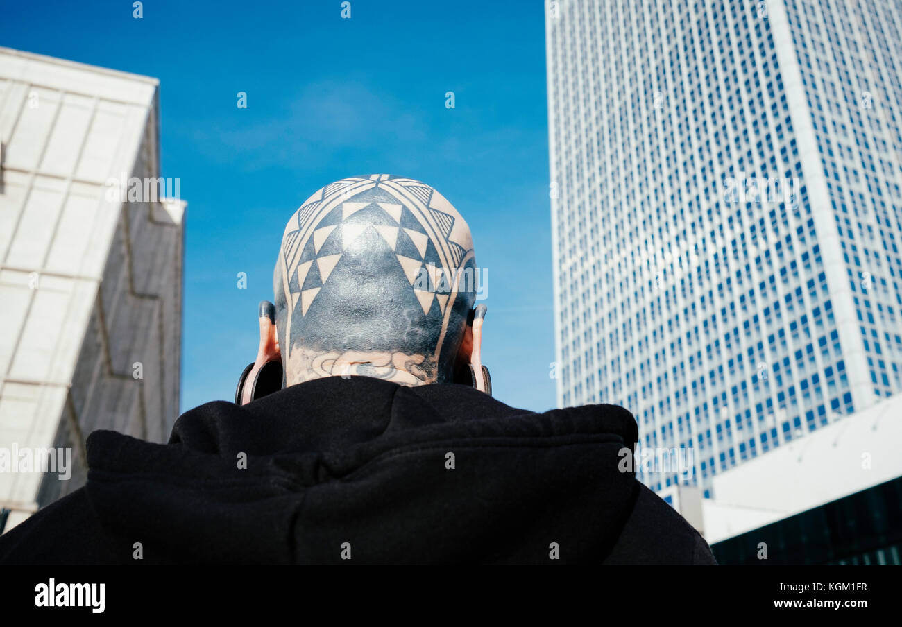 Low Angle Rückansicht des Menschen mit Tätowierungen und Ohrenstöpsel gegen Wolkenkratzer in der Stadt Stockfoto